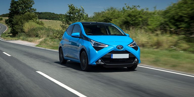 Compact, pale blue Toyota hire car being driven along a country lane.