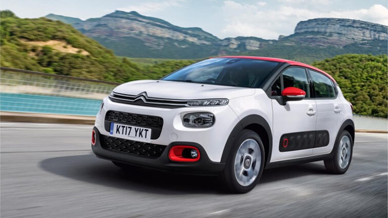 Sporty, white and red Citreon rental car, driving in a national park setting beside a lake and mountains.