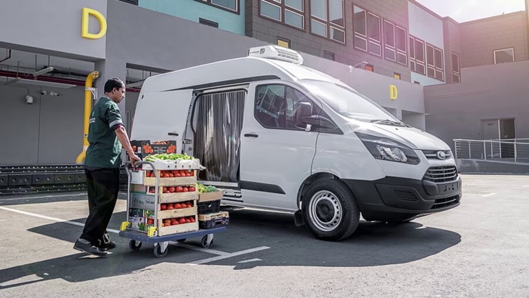 White refrigerated van being loaded up by an employee with pallets of fruit and vegetables.